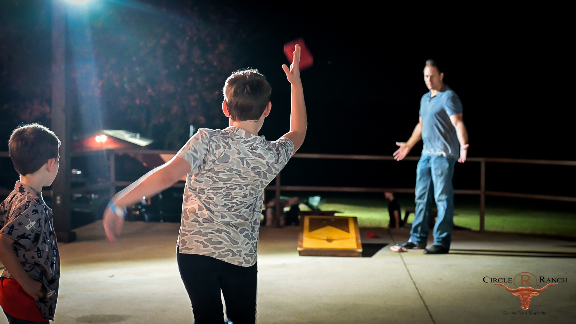 Kids playing cornhole outside at night
